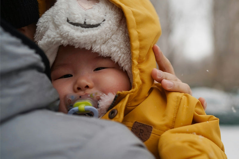 bébé emmitouflé dans un manteau jaune dans les bras d'un adulte